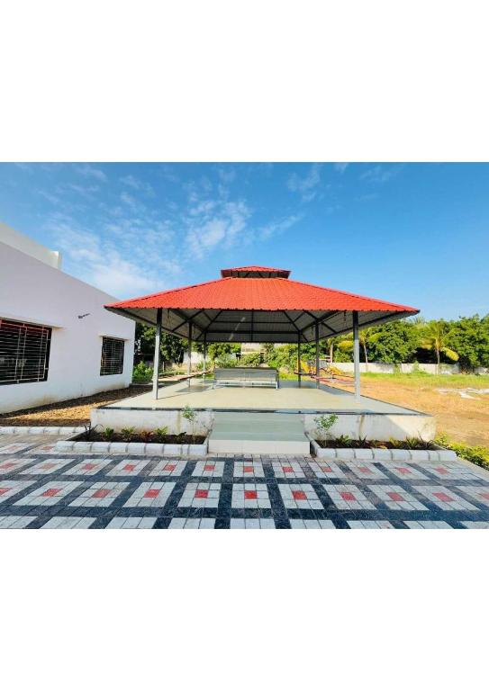 a pavilion with a red roof next to a building at Grey Stone Farm House in Surat