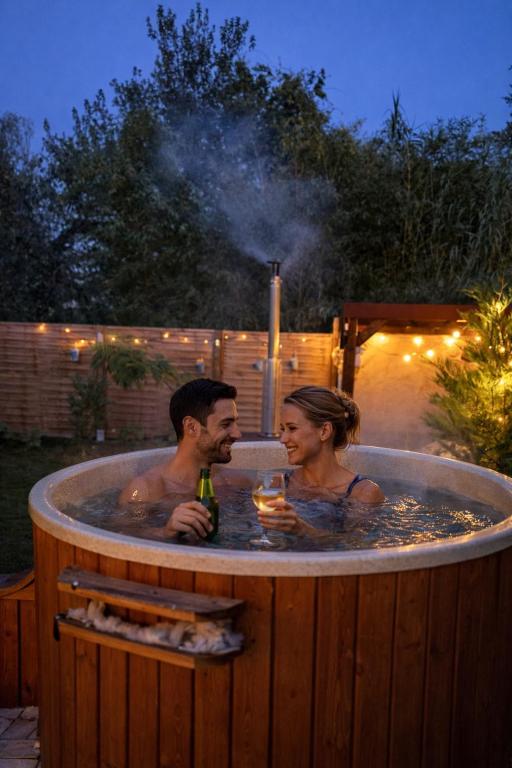 a man and a woman in a hot tub with drinks at Gesztenyeház guest house with hot tub in Leányfalu