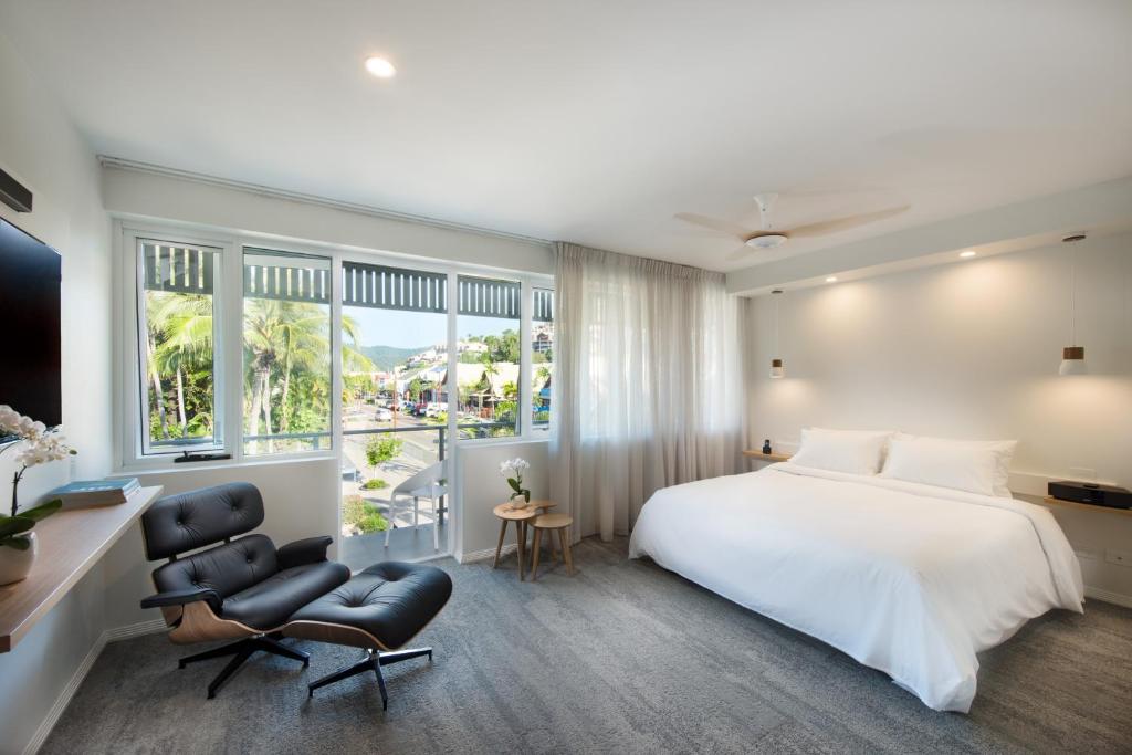 a bedroom with a white bed and a chair and windows at Heart Hotel and Gallery Whitsundays in Airlie Beach