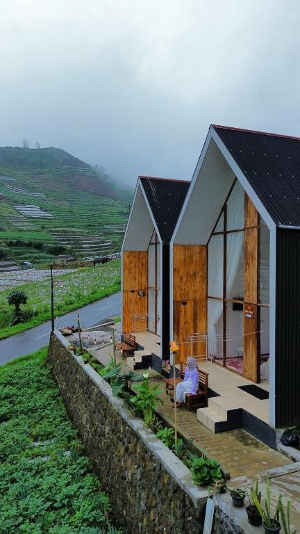 a small house with a person sitting on the porch at Pijar Jingga Cabin in Diyeng