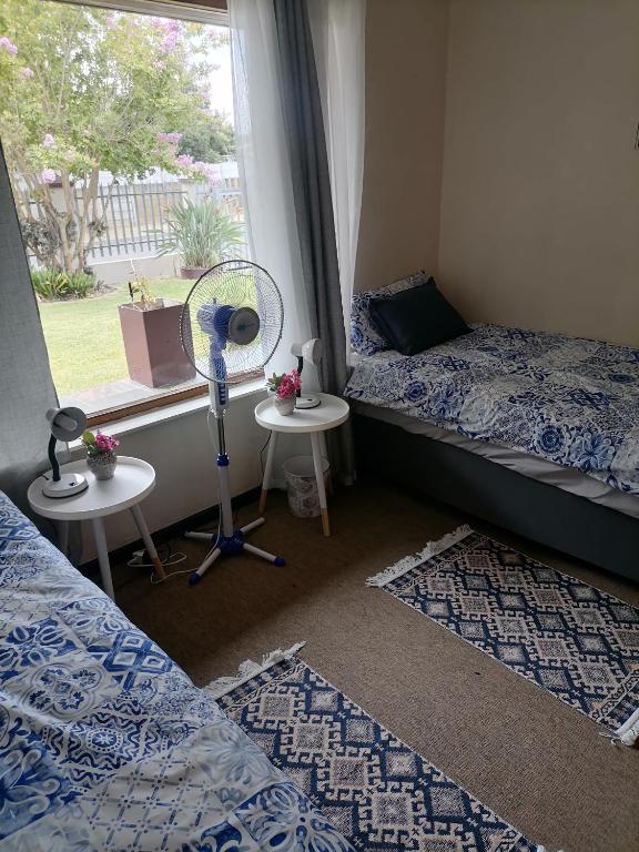 a room with two beds and a window with a fan at Mimosa House Twin Room in Brackenfell