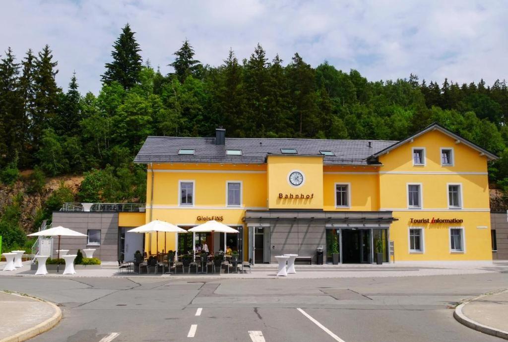 a yellow building with tables and umbrellas in front of it at GleisEiNS in Naila