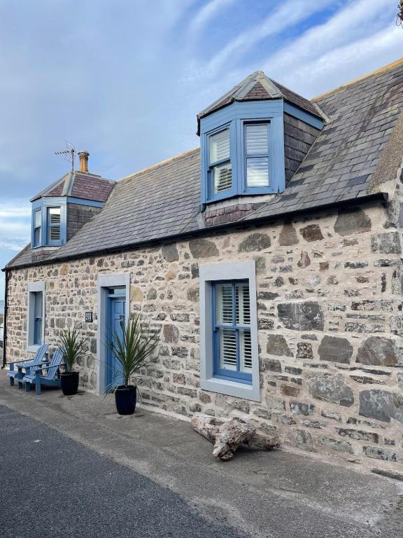 a stone house with blue windows and a bench at Sea Crest - Beachfront Escape with Whisky Snug in Cullen