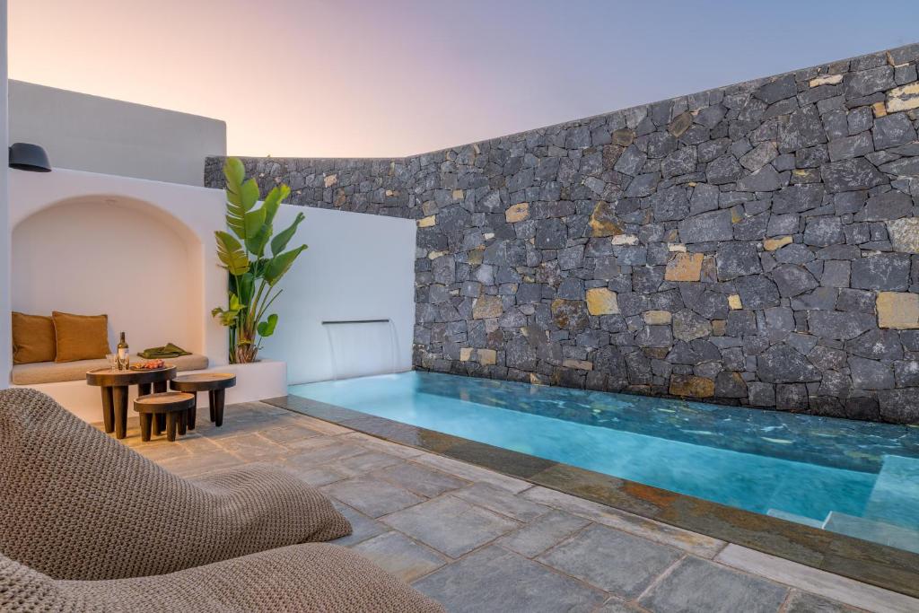 a swimming pool in a room with a stone wall at Koniko Santorini Private Pool Villas in Vóthon