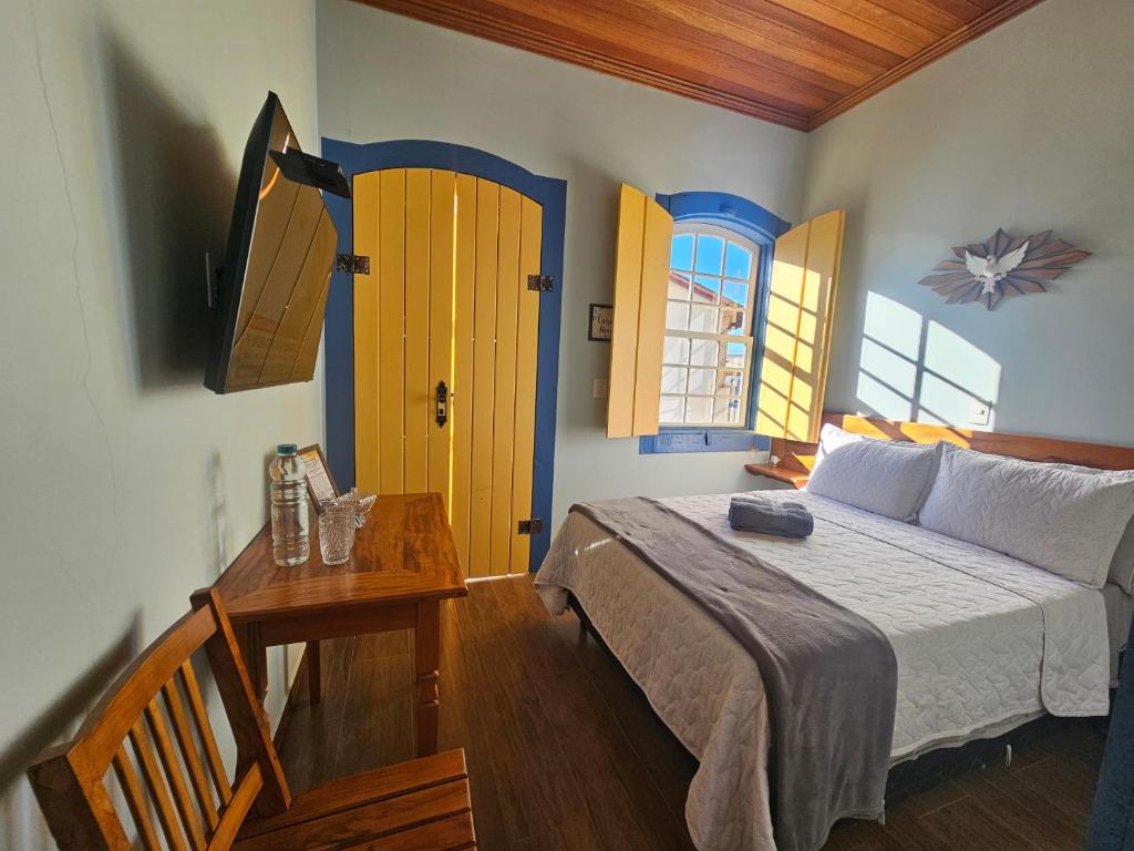 a bedroom with a bed and a table and two windows at Solar das Oliveiras in Ibertioga
