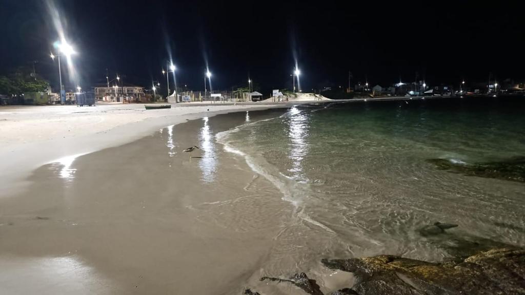 a beach at night with lights on the water at Pousada JP in Palhoça