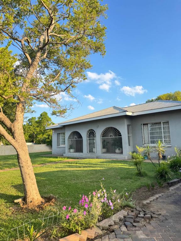 a house with a tree and flowers in the yard at SashMc Flair Guesthouse in Klerksdorp