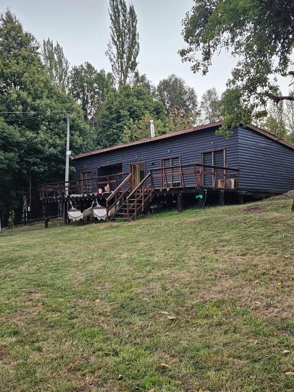 a large black building with wooden stairs and a grass field at Casa en Panguipulli in Neltume