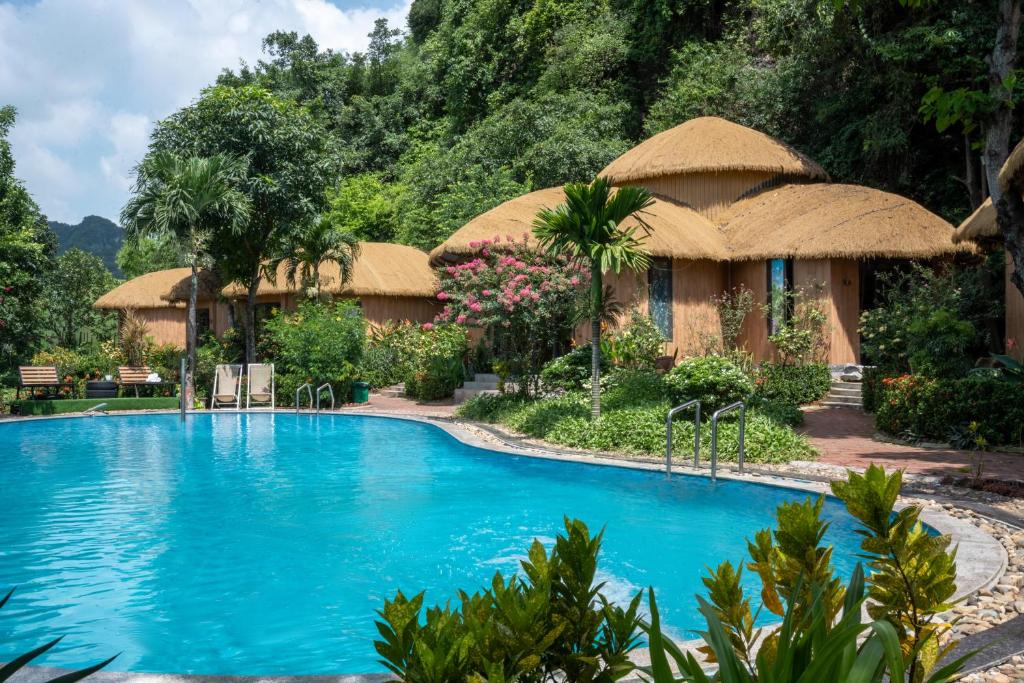 a resort with a large blue swimming pool with a thatched building at Trang An Legend in Ninh Binh