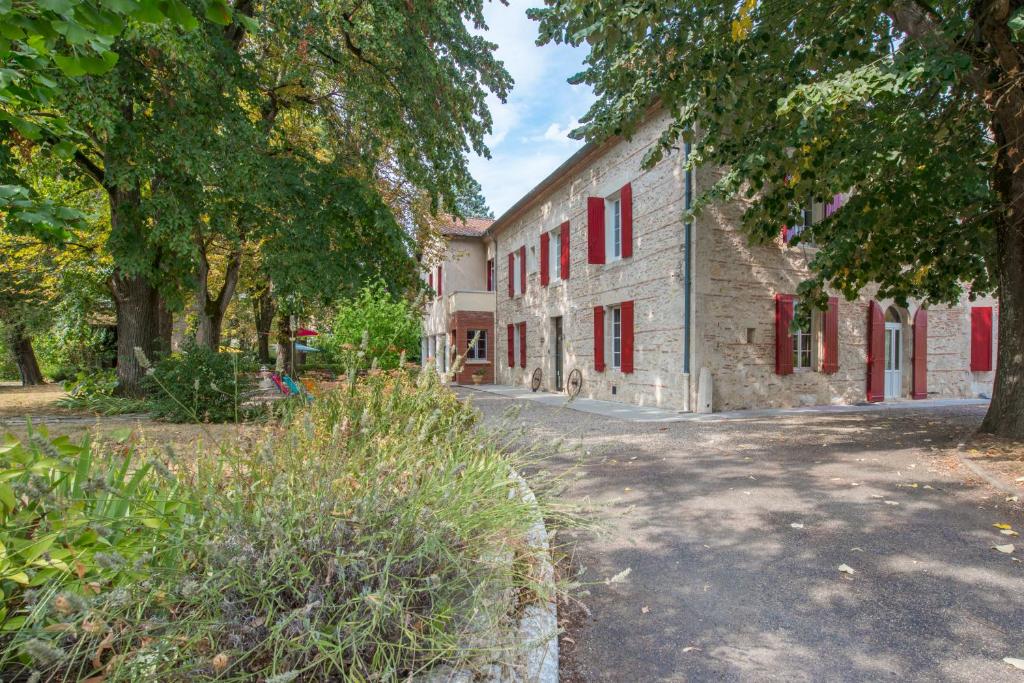 an old stone building with red windows and trees at Logis Hotels - Au Colombier du Touron in Brax