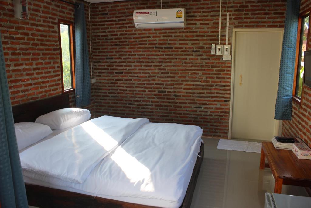 1 dormitorio con cama blanca y pared de ladrillo en Baan Suan La Moon en Chiang Khan