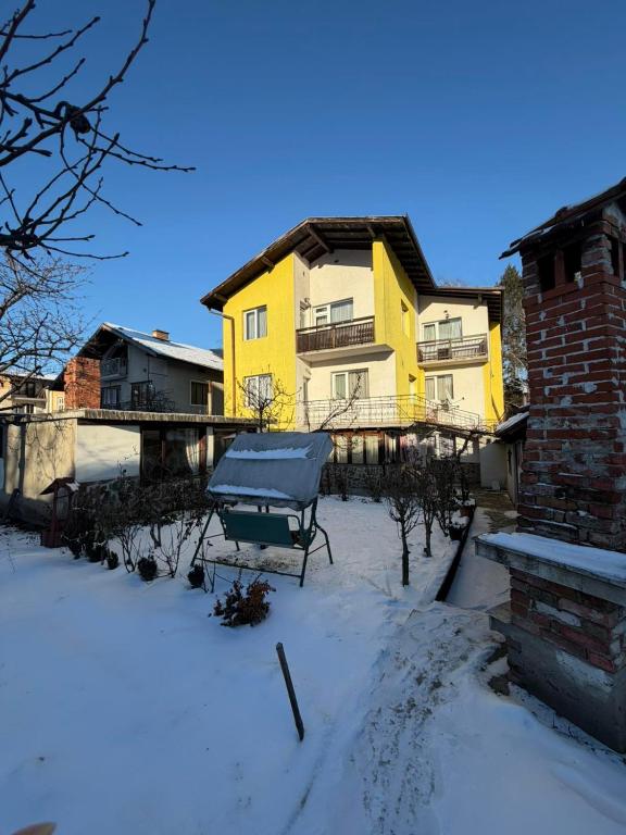 a snow covered yard with a yellow house at къща Солунови in Dobrinishte