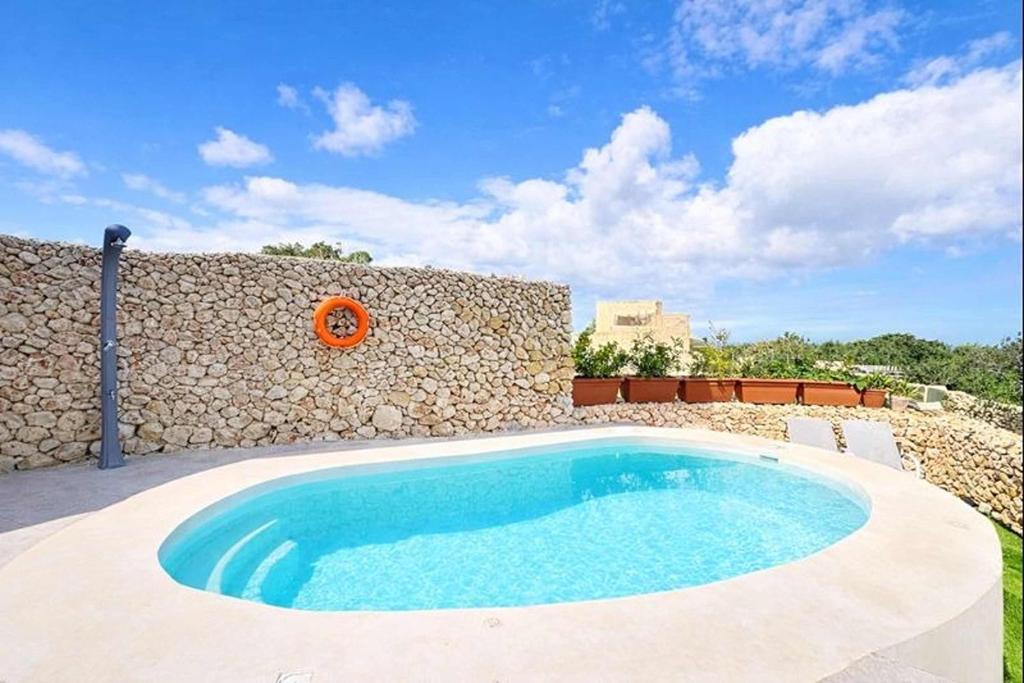 a swimming pool in front of a stone wall at Peaceful Home with Private Pool and Rooftop Jacuzzi in Xagħra