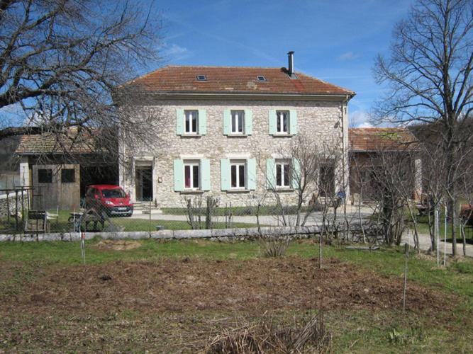 une grande maison en pierre avec une voiture rouge devant elle dans l'établissement Gîtes des Gabriels, à La Chapelle-en-Vercors