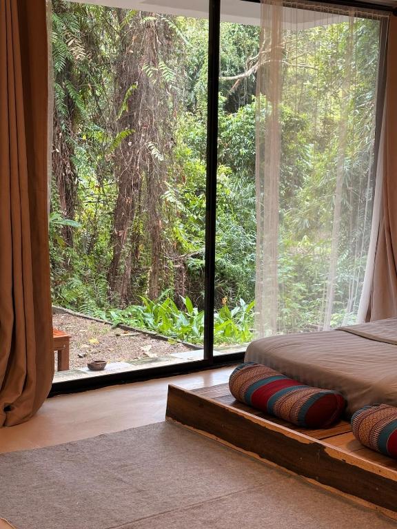 a bedroom with a large window looking out into a forest at Lakehouse in the Old Rainforest in Ko Phangan