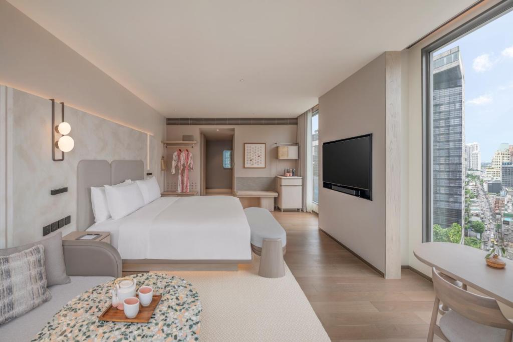 A bright bedroom-lounge with a large bed, television and floor-to-ceiling city window.