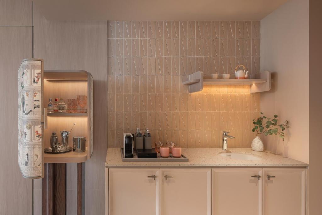 A compact kitchenette with a sink, refrigerator, coffee station and storage cabinets.