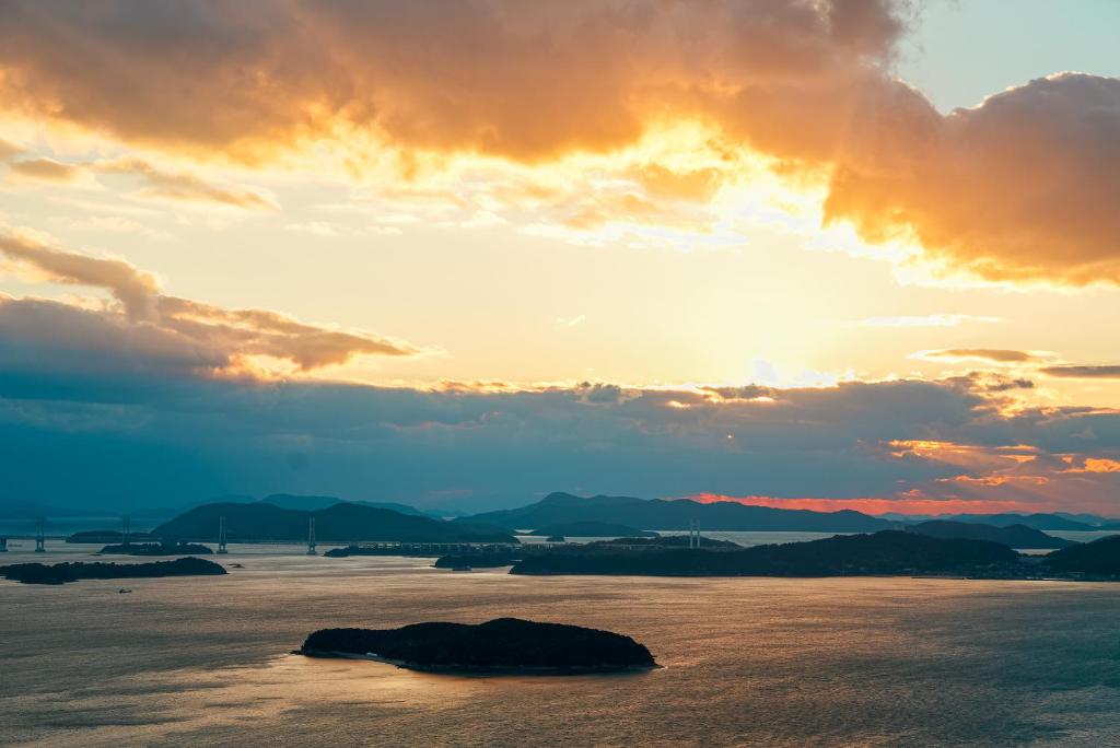 a sunset over the ocean with a rock in the water at The Nature Uno 2026年リノベーション 直島好アクセス 古民家一棟貸切 最大4名2ldk平家 クイーンベッド2台 in Tamano