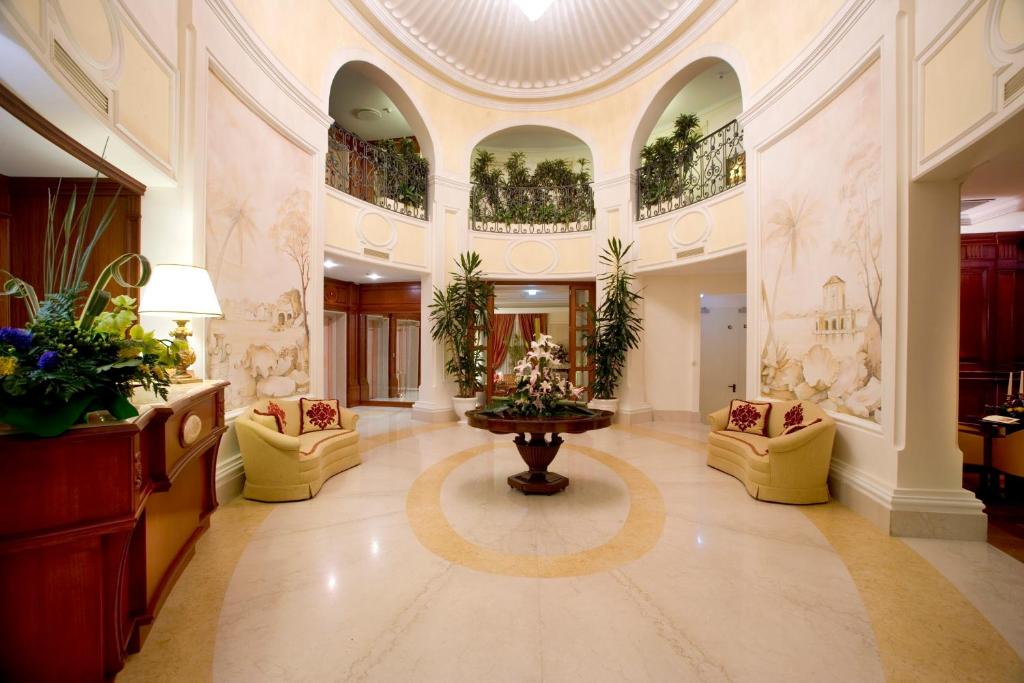 Elegant hotel lobby with round table, floral centerpiece, beige sofas, tall plants, and decorative wall murals