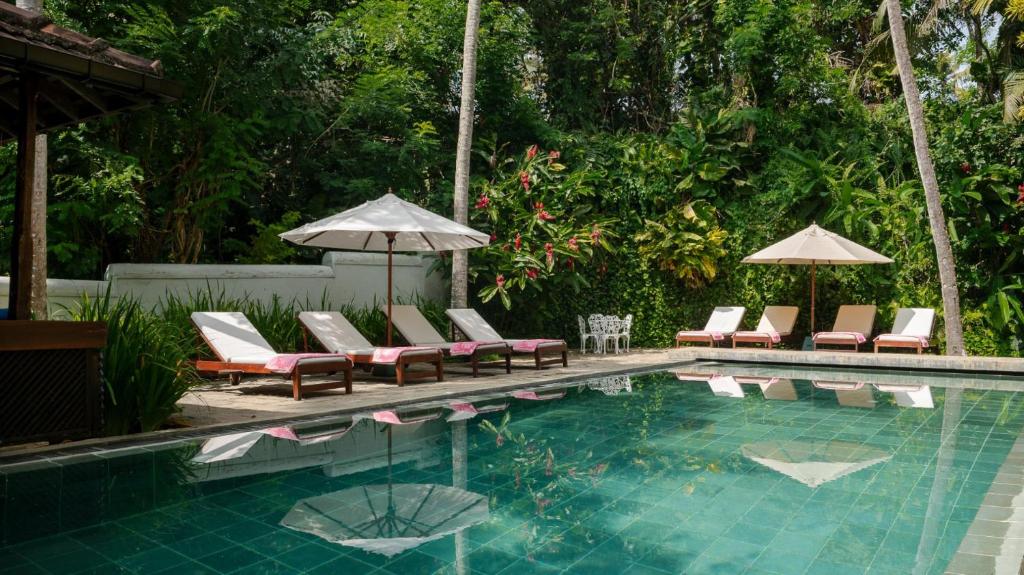 a swimming pool with lounge chairs and umbrellas next to a pool at Coconut Grove - 4 Bed Pool Villa with Cook in Ahangama