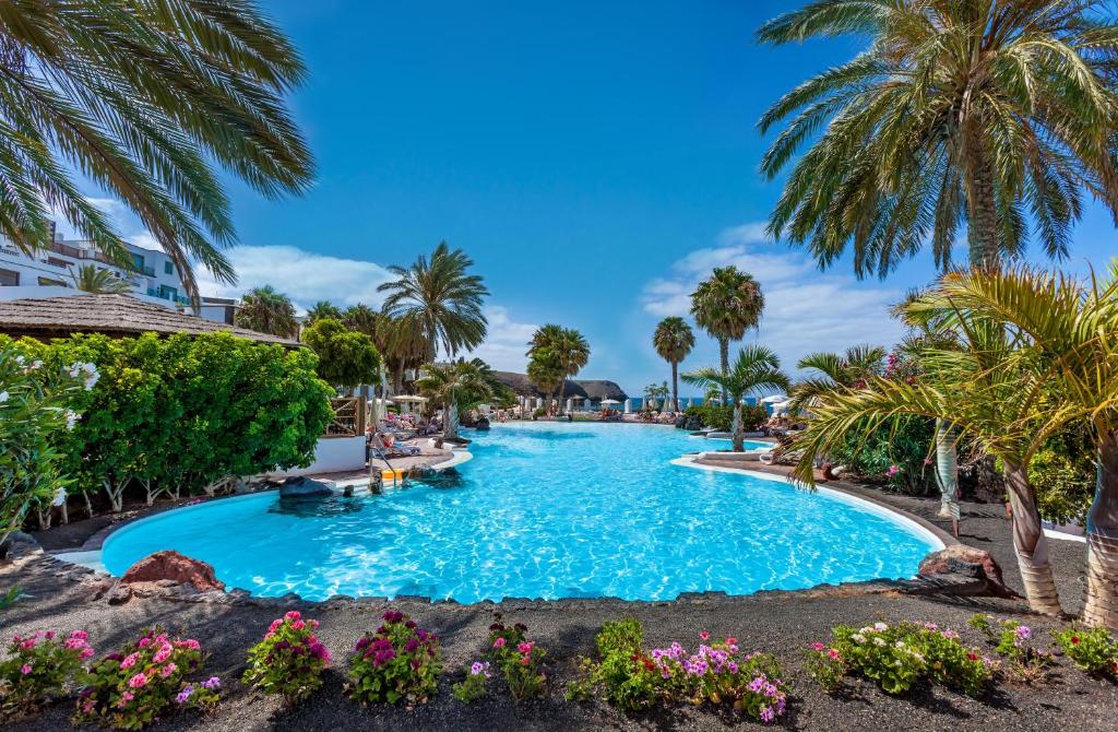 ein Pool in einem Resort mit Palmen und Blumen in der Unterkunft Gran Tagoro Family & Fun Playa Blanca in Playa Blanca