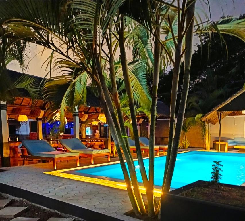 a pool with a palm tree and lounge chairs at Khair Lodge Ambanja in Ambanja