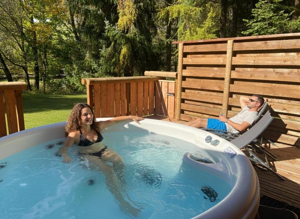 a man and woman sitting in a hot tub at LE GRIZZLY Chalet en bois avec SPA Jacuzzi in La Bresse