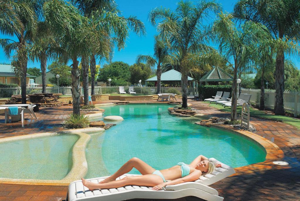 a woman laying on chairs in a swimming pool at Murray Downs Resort in Swan Hill