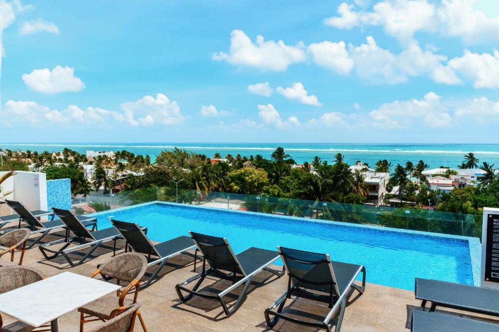 a resort pool with chairs and the ocean in the background at Areia Boutique Hotel - Puerto Morelos in Puerto Morelos