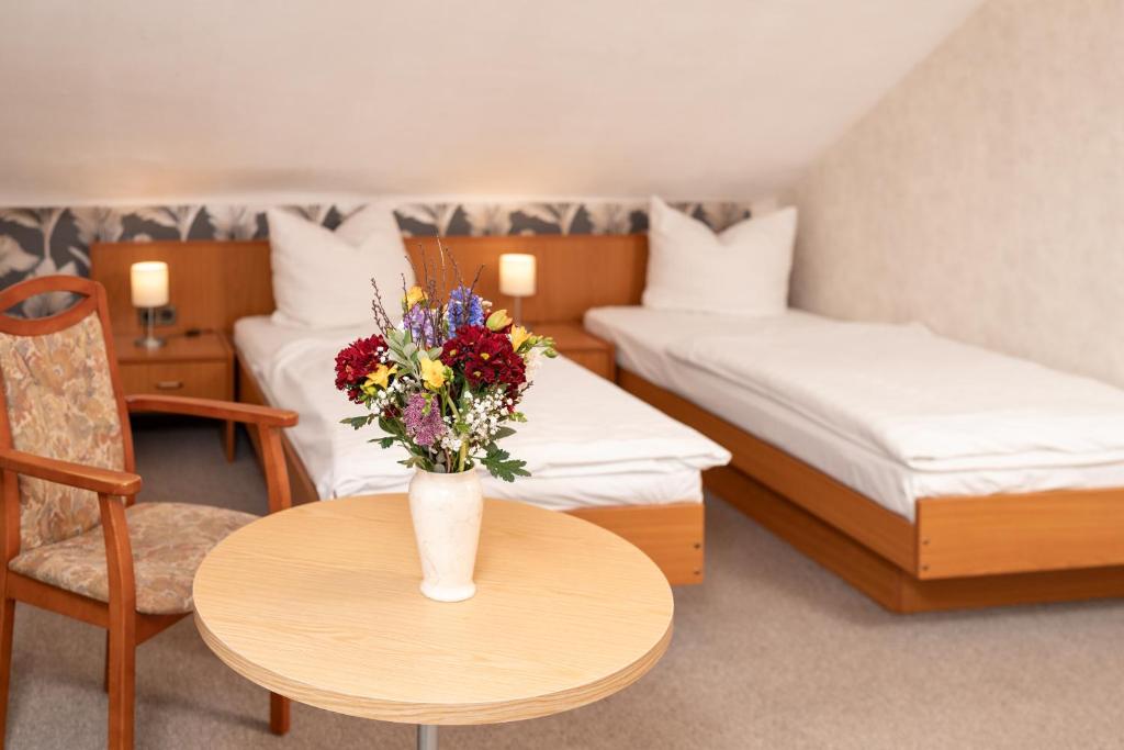 a room with two beds and a table with a vase of flowers at Hotel Waldhaus Waltershausen in Waltershausen