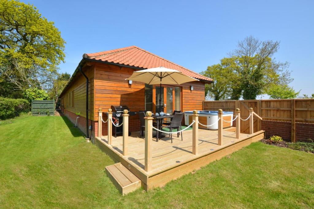 a small cabin with a deck with an umbrella at 2 Bed in Ingworth oc-1731 in Ingworth