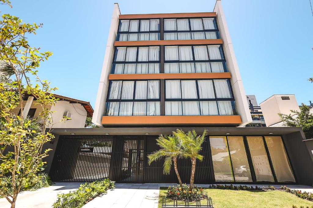 a tall building with a palm tree in front of it at Jurerê Sol&Mar Temporada in Florianópolis