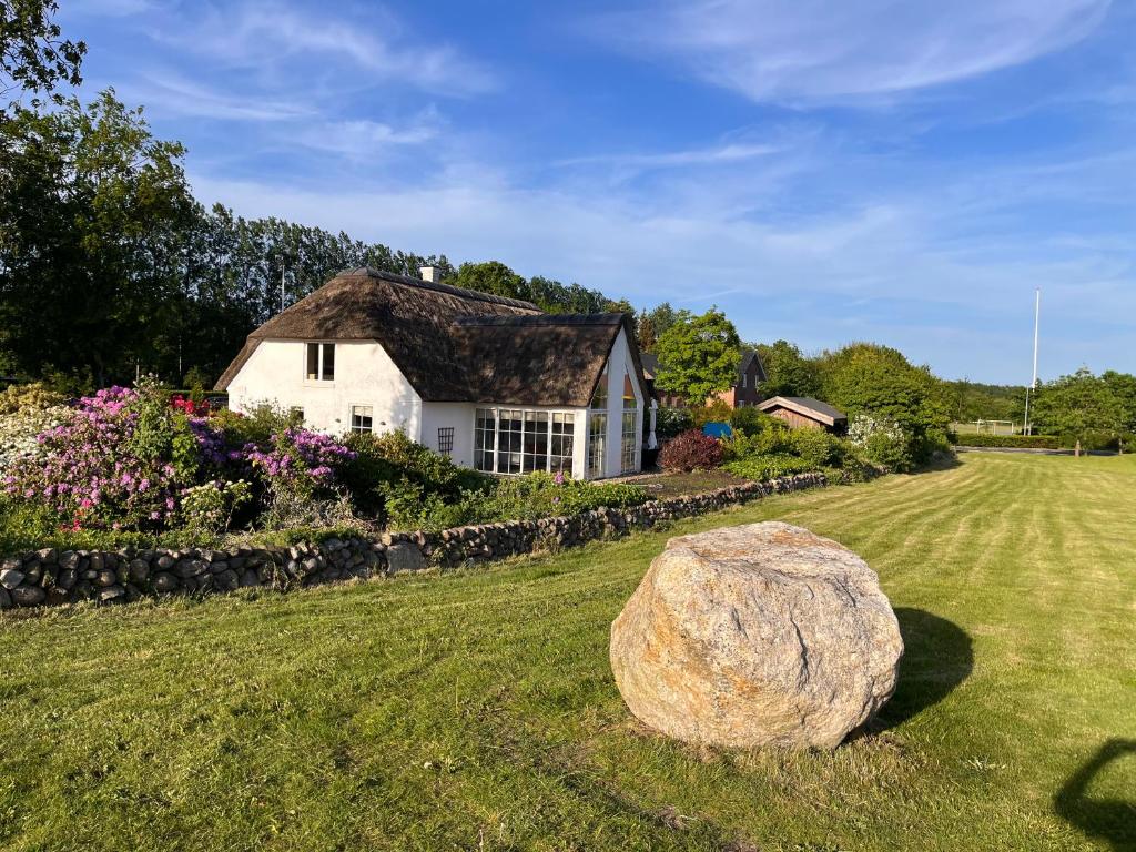 a white house with a large rock in the yard at Stråtækt Idyl in Nørre Kollund