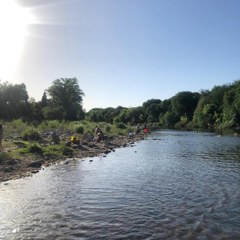 a river with a group of people sitting on the bank at Casa Aurora 1 Cosquín in Cosquín