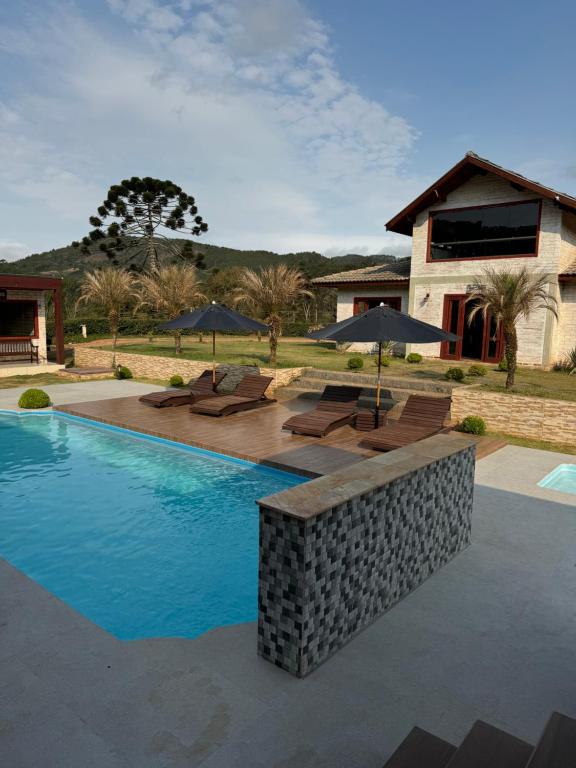 a pool with chairs and umbrellas next to a house at Pousada Villarejo in Monte Verde