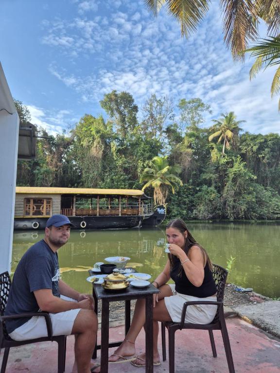 a man and woman sitting at a table near a river at BirdScapes Kumarakom Homestay in Kumarakom