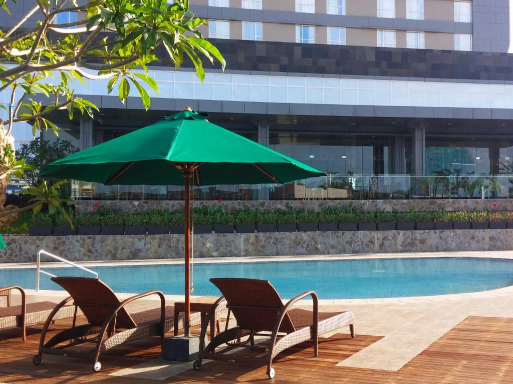 a green umbrella and chairs next to a pool at Gammara Hotel Makassar in Makassar