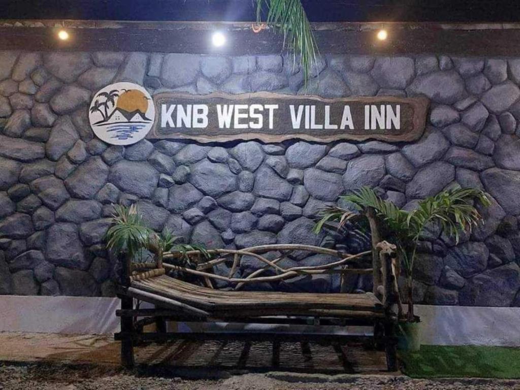 a bench in front of a stone wall with a street sign at KNB West Villa Inn by SMS Hospitality in Bolinao
