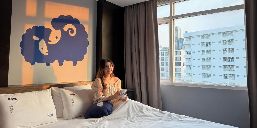 a woman sitting on a bed in a hotel room at Kokotel Bangkok Dheva Thonglor in Bangkok