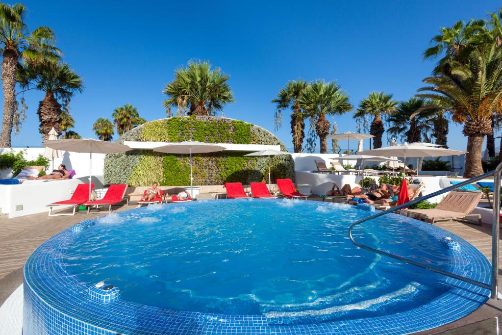a large swimming pool with red chairs and palm trees at Tigotan Lovers & Friends Playa de las Americas - Adults Only (+18) in Playa de las Americas