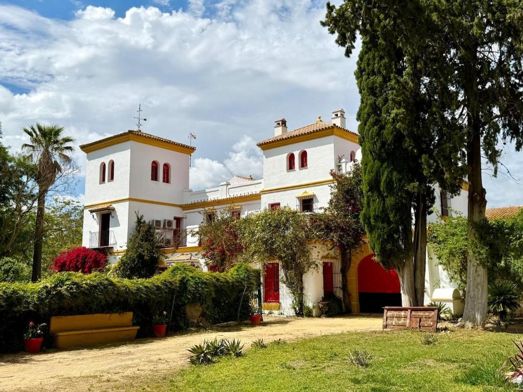 a large white house with red windows and trees at Hacienda Don Rodrigo in Alcalá de Guadaira
