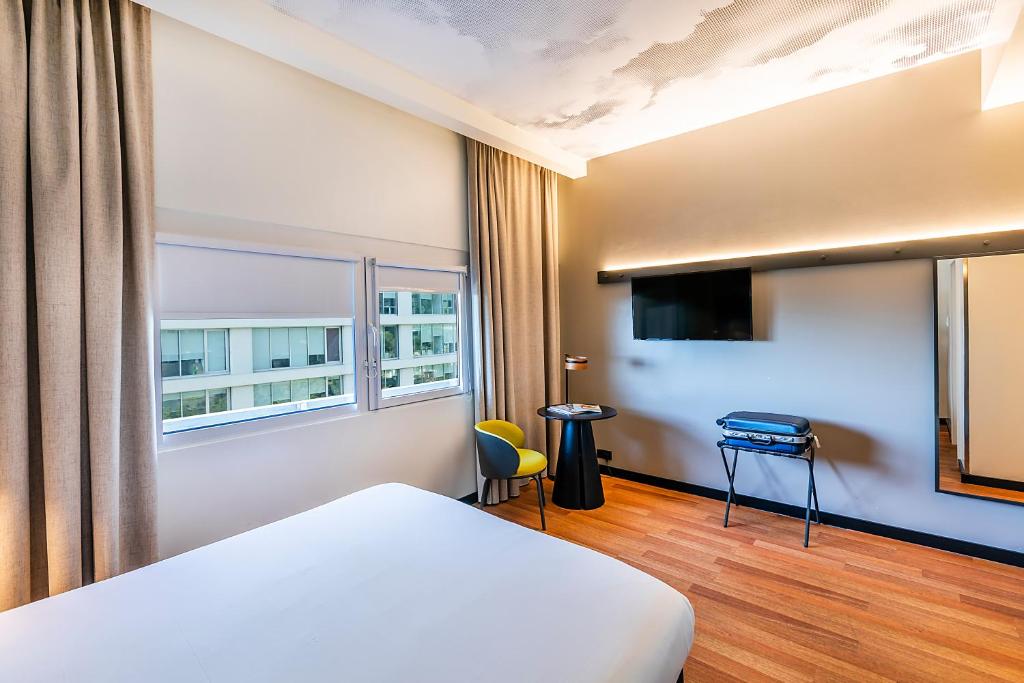 A bright guest room with a large bed, window, television and small seating area.