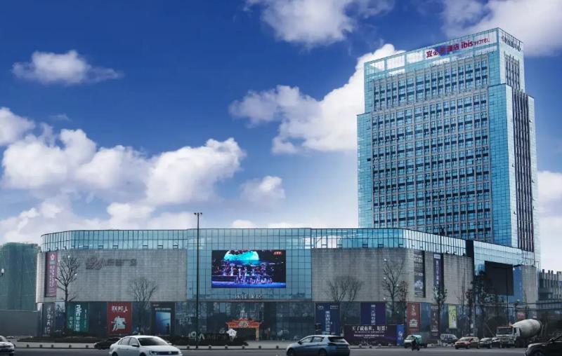 a large glass building with a billboard in front of it at Ibis Dujiangyan in Dujiangyan
