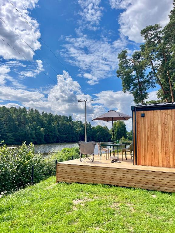 a wooden deck with a table and an umbrella at Tinyhouse Seeträumchen direkt am See mit Terrasse für 4 in Bodenwöhr