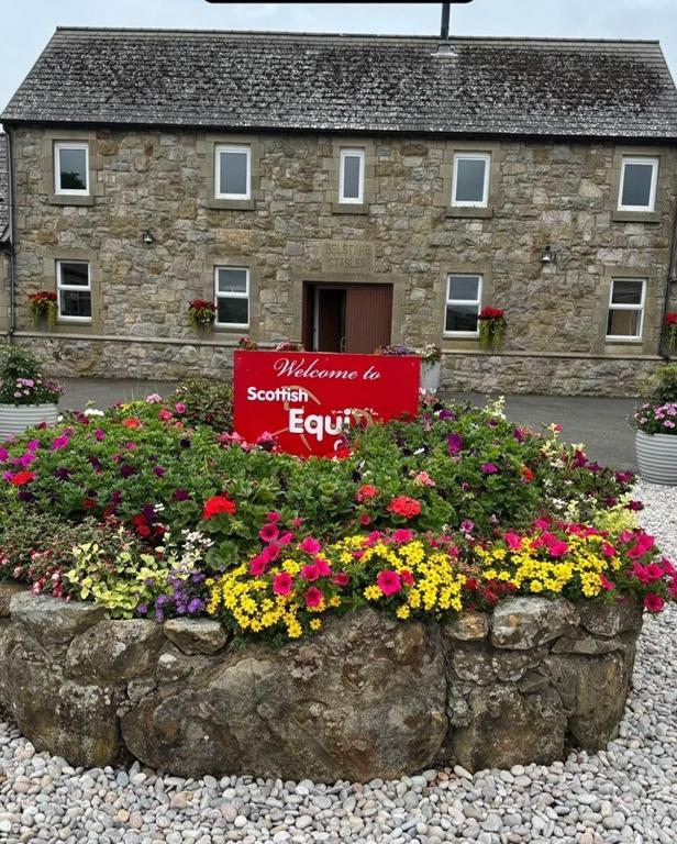Ein Schild vor einem Steingebäude mit Blumen in der Unterkunft Belstane Manor in Carluke