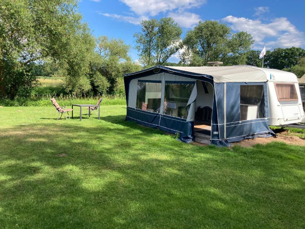 a tent in a field with a table and chairs at Mietwohnwagen E2 am Flussufer in Wienhausen