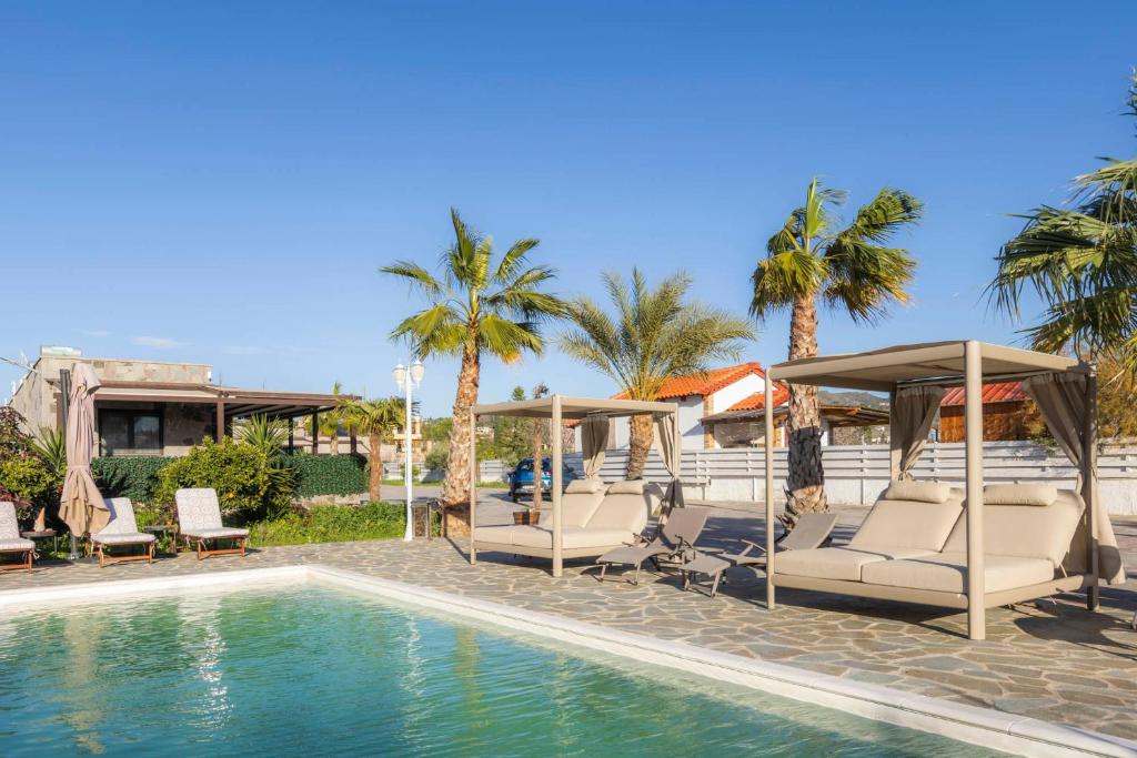 a pool with chairs and umbrellas and palm trees at Adonis Resort & Spa in Egina