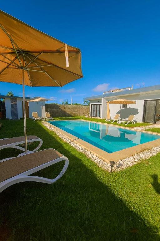 a swimming pool with an umbrella and a house at Ivy Villa Cabarete, fully equipped villa in Cabarete