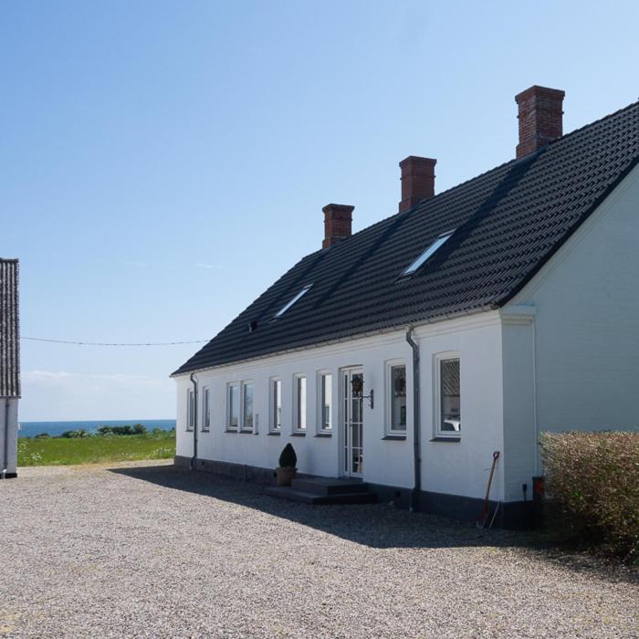 a white building with a black roof and the ocean at Sommerliv Bed and Breakfast in Tranekær