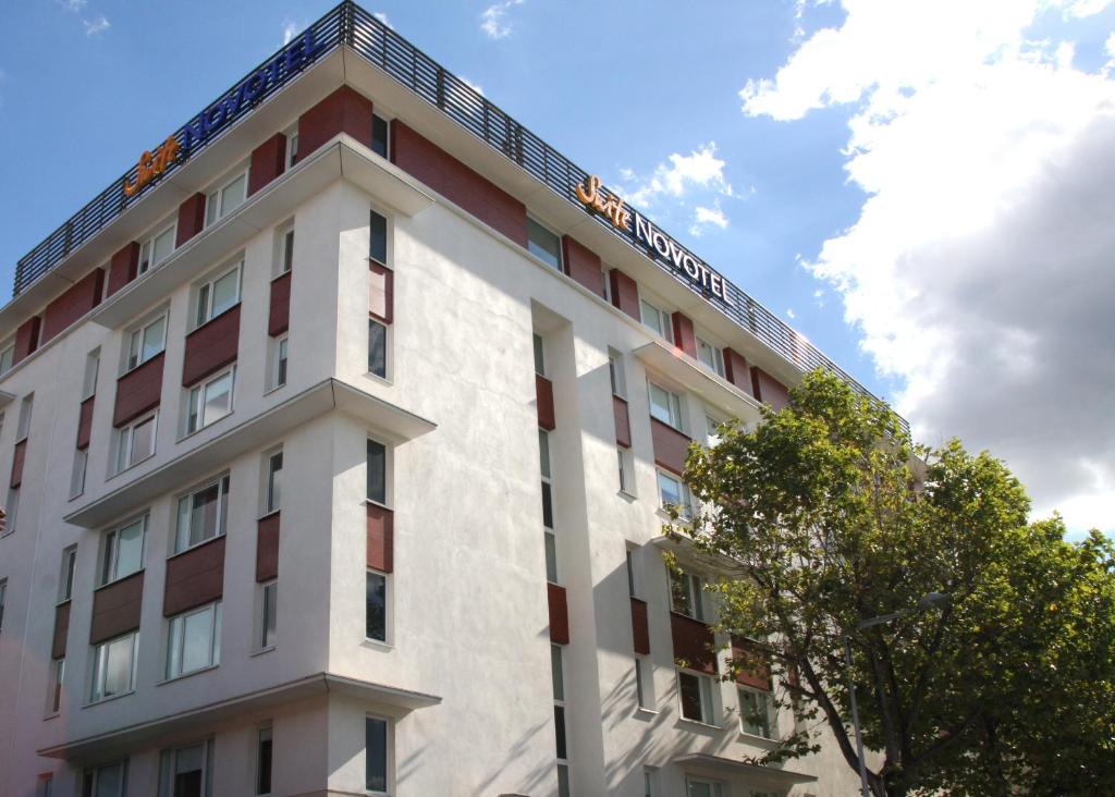 un edificio blanco y rojo con un árbol en Novotel Suites Clermont Ferrand Polydome en Clermont-Ferrand